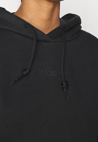 Zwarte hoodie van katoen, met een voorzak in kangoeroestijl, trekkoorden en geborduurde merkopdruk op de borst. Effen textuur.