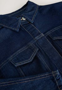 Mørkeblå denimjakke med spidse lapeller, frontlommer med klap og kontrasterende orange syninger på en lys baggrund.
