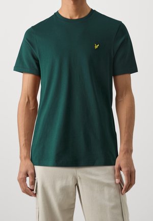 T-shirt en coton vert à manches courtes, col rond, avec un petit logo d'oiseau jaune sur la poitrine gauche. Texture lisse, coupe régulière.