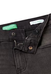 Jeans ajustados negros con cierre de cremallera y botón, con etiquetas de United Colors of Benetton y Kanye-Skinny. Material de denim texturizado.
