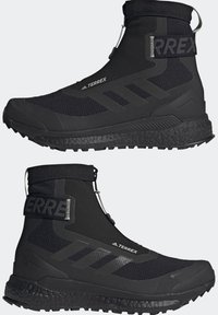 Bottes de randonnée Adidas Terrex noires de hauteur moyenne avec semelles texturées, fermeture éclair et bride velcro à la cheville, vues de côté.