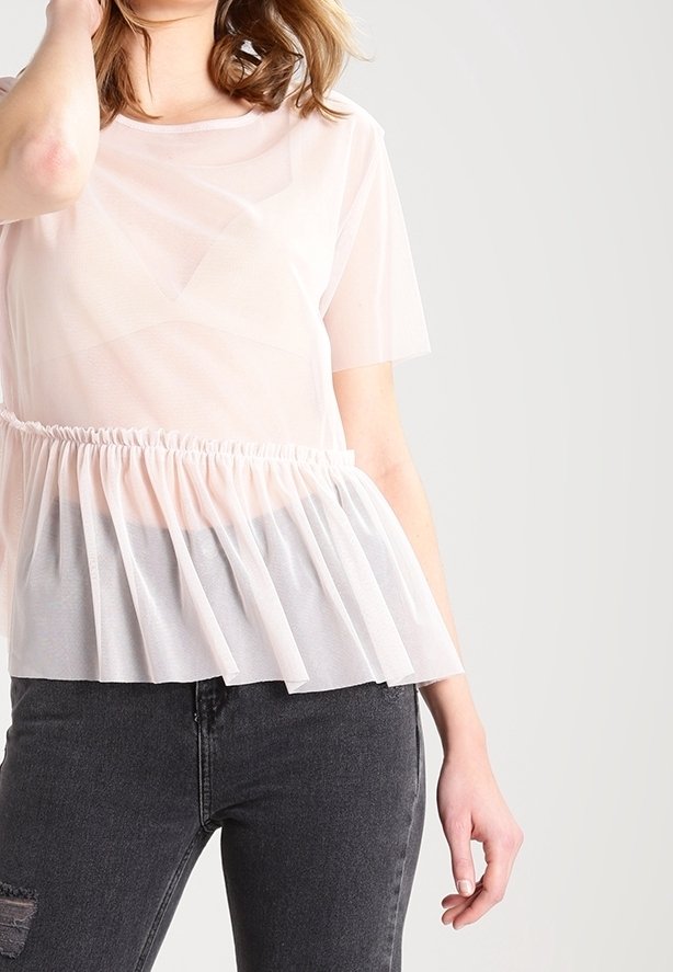 Světle růžové tričko s průhlednou vrstvou, krátkými rukávy a nařaseným tylovým lemem. Nošeno s tmavými džíny, má kulatý výstřih a jemnou texturu.