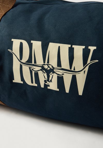 Kék vászontáska, amelyen nagy krém színű "RMW" felirat és egy hosszú szarvú bika koponya grafika található, barna díszítéssel. Tartós anyag, amelynek textúrált felszíne van.