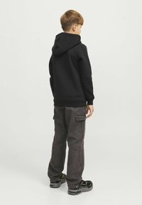 Felpa nera con una texture morbida e un grande cappuccio, abbinata a pantaloni cargo scuri con tasche laterali e una vestibilità ampia.