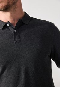 Polo triko v uhlově šedé barvě s dlouhými rukávy, zapínací límec, strukturovaná tkanina a viditelné švy u légy.