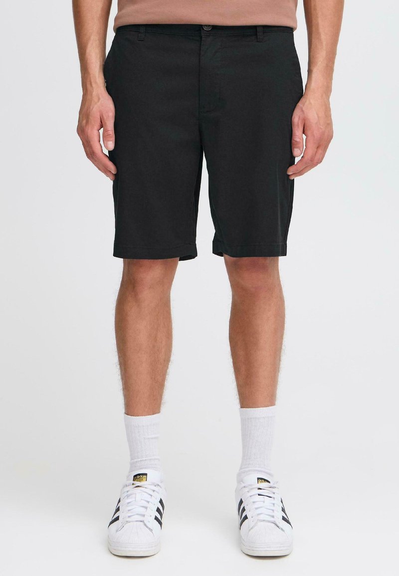 Black shorts with a straight cut, made of lightweight fabric. Features front pockets and a button closure. Worn with white socks and sneakers.