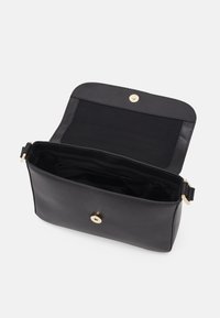 Sacoche en cuir noir avec rabat ouvert, montrant un intérieur spacieux et une fermeture à bouton magnétique doré.