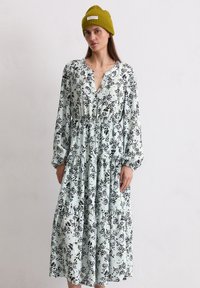 Blumenmuster-Kleid in Hellblau mit schwarzen und gelben Akzenten, mit einer Knopfleiste vorne, langen Ärmeln und einem schichtweisen Rock.