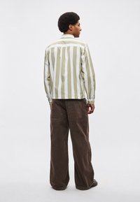 Ριγέ πουκάμισο σε πράσινο και λευκό, με μακριά μανίκια και κουμπωτό μανσέτα. Καφέ παντελόνι κοτλέ με φαρδιές παντελόνι και δύο πίσω τσέπες.