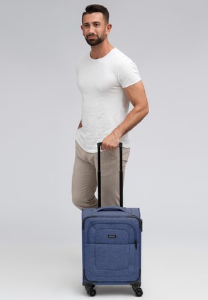 Maleta de mano de tela azul con un asa reforzada, ruedas suaves y bolsillos con cremallera en la parte frontal; dimensiones adecuadas para viajar.