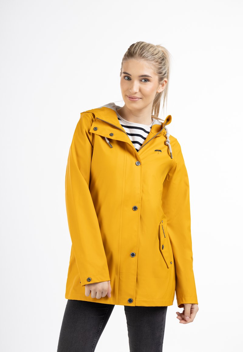 Giacca impermeabile gialla con cappuccio, caratterizzata da una cerniera frontale e bottoni a pressione, e tasche laterali. Camicia a righe visibile sotto.