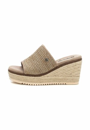 Sandalia de cuña con parte superior de tela beis trenzada, puntera abierta y suela texturizada estilo espadrille. Presenta un acento decorativo metálico.
