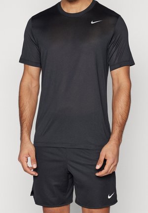 Mann trägt schlichte schwarze Nike-Kurzarmshirt und passende schwarze Nike-Shorts vor einfarbigem Hintergrund.