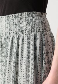 Šviesiai pilkas sijonas su guminiu juosmeniu. Pasižymi tamsiomis gėlių ir deimantų raštais, laisvai krentančia medžiaga ir raukšlėta tekstūra.