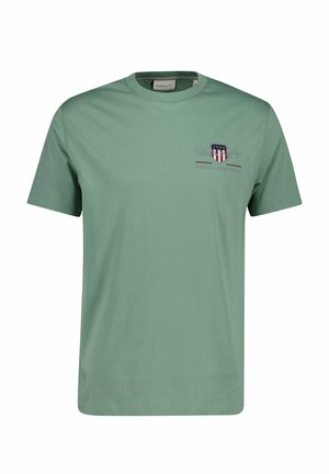 Hellgrünes T-Shirt mit kurzen Ärmeln und Rundhalsausschnitt, kleinem besticktem Schild und Textlogo auf der linken Brust, Markenetikett innen am Kragen.