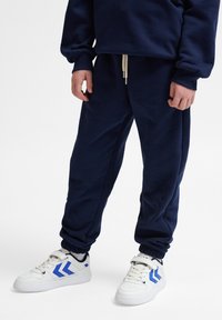 Granatowe dresy z polaru z elastycznymi mankietami i przesuwnym pasem, w połączeniu z białymi sneakersami z niebieskimi akcentami i sportowym designem.