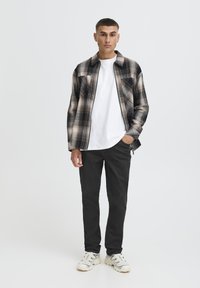 Cămașă din flanel cu un model în carouri alb-negru, purtată peste un tricou alb, asortată cu blugi închiși la culoare și adidași deschiși. Stil simplu, contemporan.