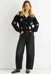 Black cardigan with colorful embroidered flowers, gold buttons, ribbed cuffs, paired with high-waisted black jeans and black ballet flats.