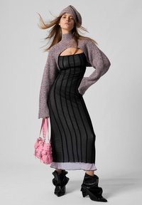 Kvinde iført en lilla strikket cropped sweater og beret, sort mesh-striped kjole med lavendelkant, sorte slouchy støvler, holder en lyserød håndtaske.