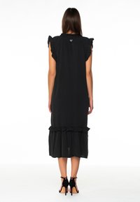 Musta mekko, jossa on röyhelöillä varustetut lyhyet hihat ja röyhelöinen helma. Valmistettu kevyestä materiaalista, takana on huomaamaton logo.