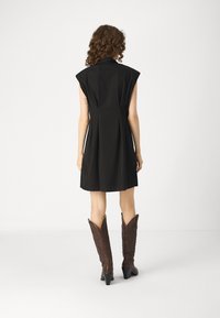 Μαύρο φόρεμα με κοντά, δομημένα μανίκια, εφαρμοστό μέσο και φαρδιά φούστα. Συνδυασμένο με καφέ καουμπόικες μπότες με λουλουδάτα σχέδια.