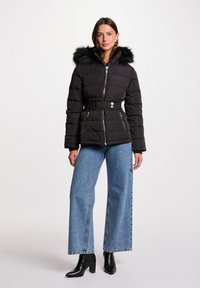 Giacca a vento nera con cappuccio in pelliccia sintetica, zip frontale, vita con cintura, tasche con zip, abbinata a jeans blu a vita alta e stivali neri con tacco.