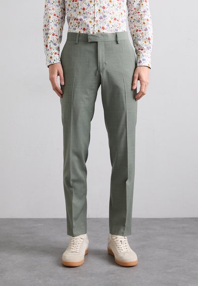 Pantalons ajustés vert clair avec une texture lisse, présentant un design à l'avant plat et des poches latérales, associés à des baskets beiges décontractées.