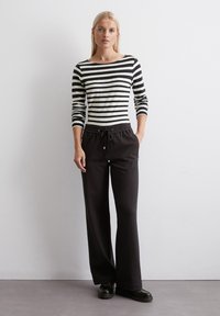 Zwarte, wijde broek met een trekkoord in de taille. Gecombineerd met een zwart-wit gestreepte lange mouwen top. Soepele stof en een ontspannen pasvorm.