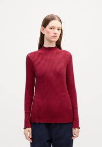 Dlhý rukáv, rebrovaný rolák v tmavočervenej farbe s vlnitým lemom a manžetami, vyrobený z elastickej látky pre fitted siluetu.
