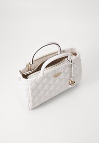 Bolso acolchado blanco con asas dobles, herrajes dorados y un compartimento con cremallera. Presenta un charm con el nombre de la marca adjunto.