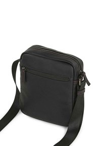 Bolso cruzado negro hecho de piel suave con cierre de cremallera, que cuenta con un bolsillo delantero con cremallera y un detalle de costura roja en contraste.