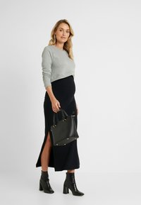 Sweater cinza cropped, saia justa preta com fenda lateral, botas de cano curto pretas com salto e uma pequena mala preta com detalhes em dourado.