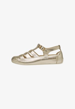 Metallisch goldene Sandalen mit offenem Design, überkreuzten Riemen, strukturiertem Finish und flacher Sohle. Mit Markennamen an der Seite.