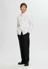 Camicia button-up con pattern a righe bianche e pastello, maniche lunghe, taschino sul petto; abbinata a pantaloni neri larghi e scarpe nere.