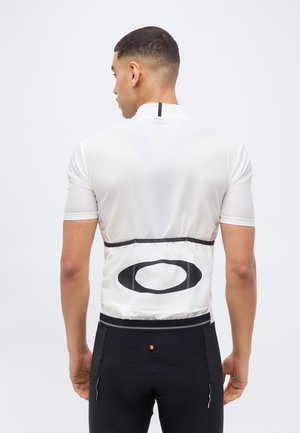 Mees, kes kannab valget rattasõidu särkigi musta ovaalse logoga alumisel seljal ja musti rattasõidu lühikesi pükse, seisab seljaga vaataja poole.