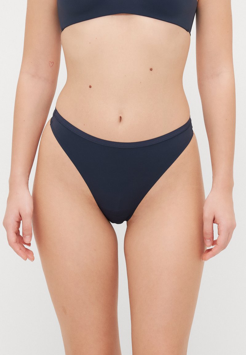 Navy blue bikini w zestawie, wykonany z gładkiego materiału; zawiera krótką bluzkę z szerokimi ramiączkami oraz niskopoprzeczne majtki w minimalistycznym stylu.