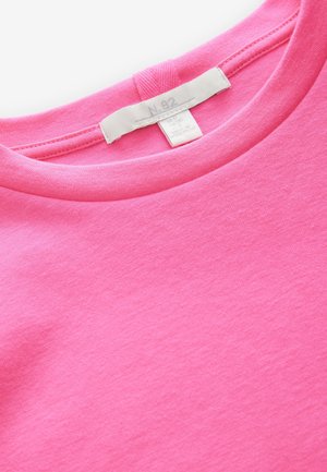 Vaaleanpunainen puuvillainen t-paita, jossa pyöreä kaula-aukko ja pehmeä koostumus. Kauluksen sisäpuolella valkoisessa nimilapussa lukee "N.82". Yksinkertainen malli ja väri.