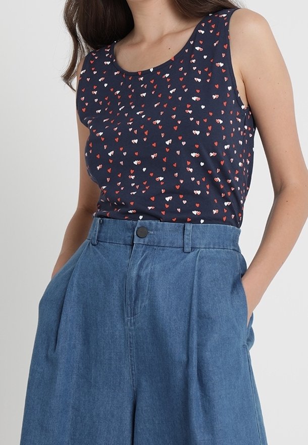 Marineblaues Tanktop mit kleinen roten und weißen Herzmustern, kombiniert mit hellblauen, hoch taillierten, weit geschnittenen Hosen mit einem Frontknopf.