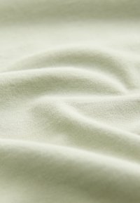 Svetlo zelena bombažna tkanina z gladko teksturo, z nežnimi gubami in fino pletenim vzorcem, ki izraža mehkobo in prožnost.