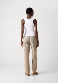 Top bianco in cotone abbinato a pantaloni beige a gamba larga. I pantaloni presentano tasche posteriori e una vestibilità rilassata, mentre i sandali completano il look informale.