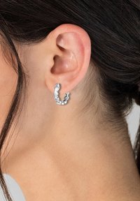 Pendientes de aro de plata con un diseño enlazado, acabado liso y pulido, y acentos circulares que muestran una estética contemporánea.