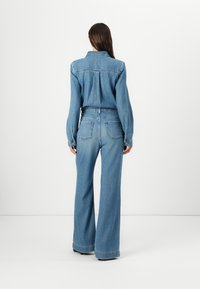 Denim odjeća koja se sastoji od košulje s dugmadi i hlača širokih nogavica. Svijetloplava boja s glatkom teksturom i stražnjim džepovima na hlačama.