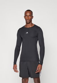 Sort langærmet træningsskjorte med tætsiddende design. Har en rund halsudskæring og et hvidt adidas-logo på brystet. Glat tekstur.