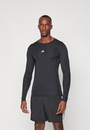 Schwarzes, langärmliges Sportshirt mit figurbetontem Design. Mit Rundhalsausschnitt und einem weißen adidas-Logo auf der Brust. Glatte Textur.