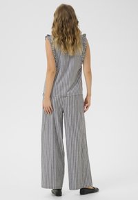 Tenue en deux pièces : haut sans manches et pantalon à jambes larges en gris avec des rayures verticales blanches, présentant des accents de manches volantées. Tissu léger.