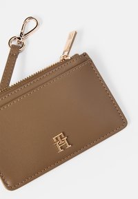 Ruskea nahkalompakko, jossa on kultaiset yksityiskohdat, vetoketjulukko, avainklipsi ja kohokuvioitu logo. Ominaisuuksina sileä pinta ja siisti tikkaus.