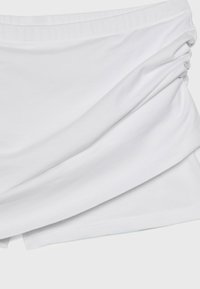 Tissu blanc avec un détail froncé sur un côté, créant un effet froncé sur un matériau lisse.