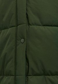Grüne, gesteppte Jacke mit weicher Textur, die über eine auffällige Knopfleiste und genähte Details entlang der Nähte verfügt.