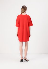 Czerwona, oversize sukienka t-shirtdo pośladków, wykonana z gładkiego materiału, z krótkimi rękawami, okrągłym dekoltem i luźnym krojem, w zestawieniu z czarnymi, sznurowanymi szpilkami.