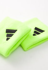 Neónovo zelené atletické zápästné pásky vyrobené z textúrovaného materiálu, na každom pásku s čiernym trojuholníkovým logom pre branding.